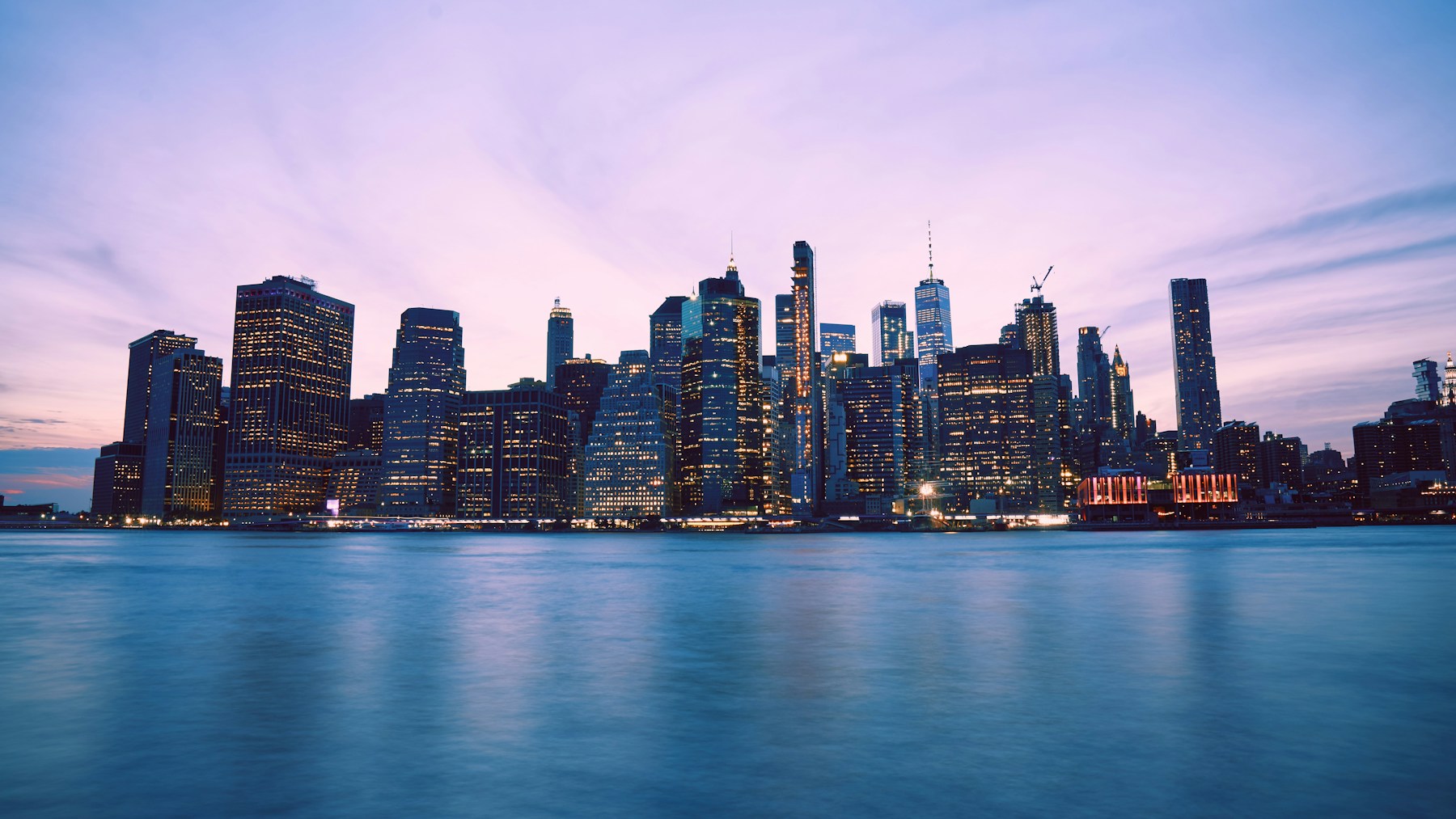 Manhattan skyline at blue hour across water; panoramic